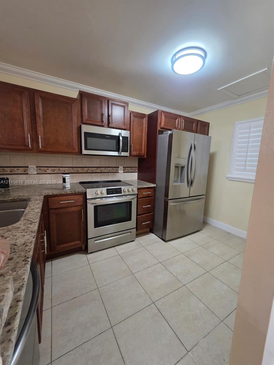 Kitchen featuring stained wood cabinetry, stone-surface countertops, stainless steel appliances, and ceramic tile flooring