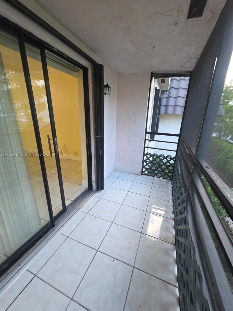 Covered balcony featuring square tile flooring, black metal railing with lattice detailing, and sliding glass door access