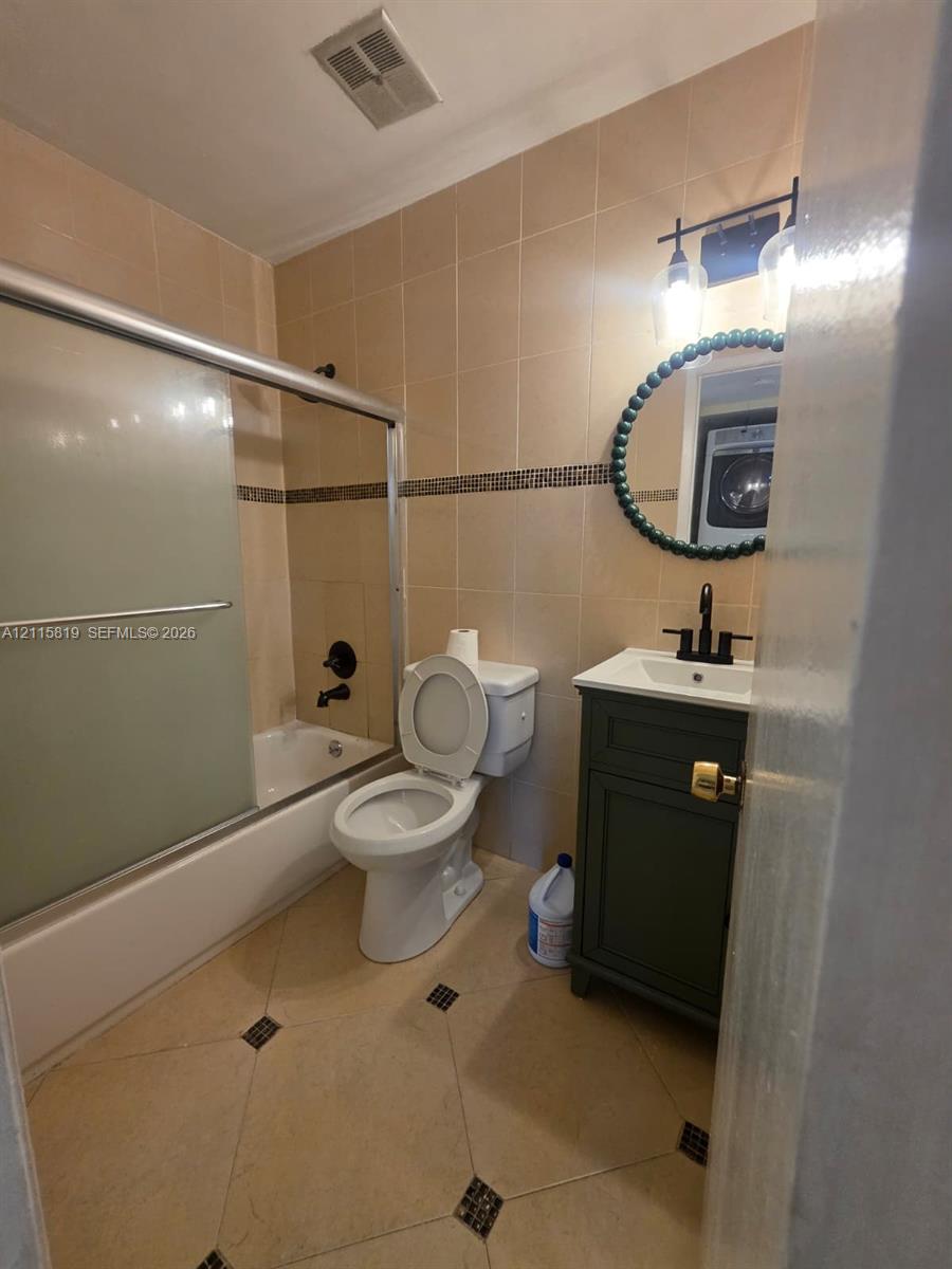 Bathroom featuring a vanity with a white countertop and dark cabinetry, a soaking tub with a sliding glass door, a matte black faucet, and stone-finish floor tiling with decorative inserts