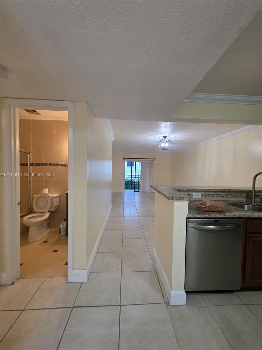 Kitchen featuring stone-finish countertops, stainless steel dishwasher, and dark wood-finish cabinetry, complemented by uniform tile flooring and crown molding throughout the interior