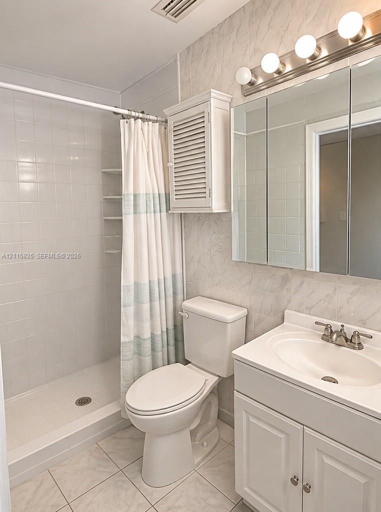 Bathroom featuring a tiled walk-in shower with integrated shelving, white vanity with an integrated sink, three-panel medicine cabinet, and wall-mounted light fixture