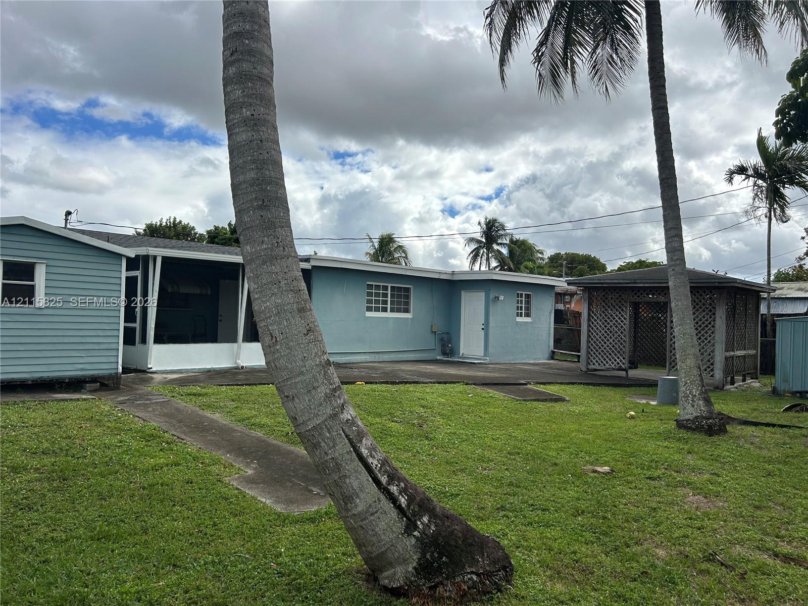 Exterior featuring light blue lap siding, a screened-in porch, a detached wood-lattice gazebo, and expansive lawn area with mature palm trees