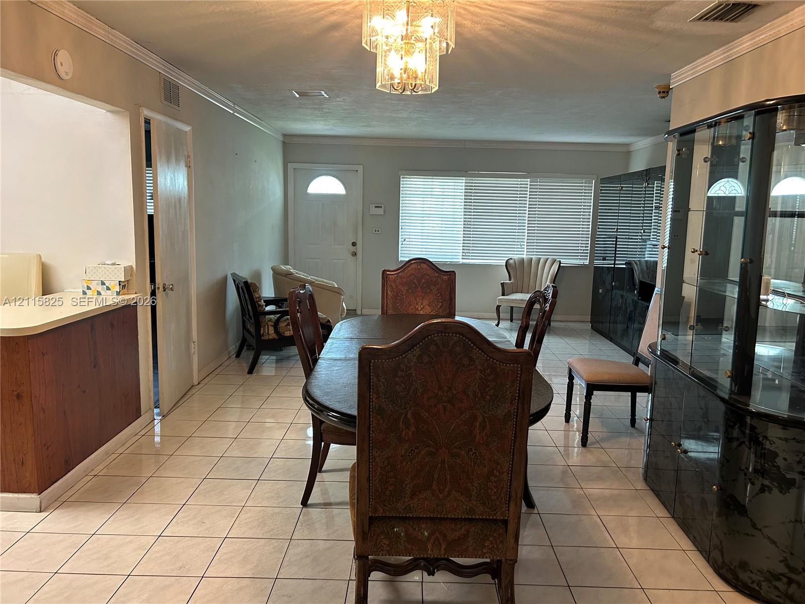 Open-concept interior featuring light-toned tile flooring, recessed crown molding, and a multi-tiered crystal chandelier