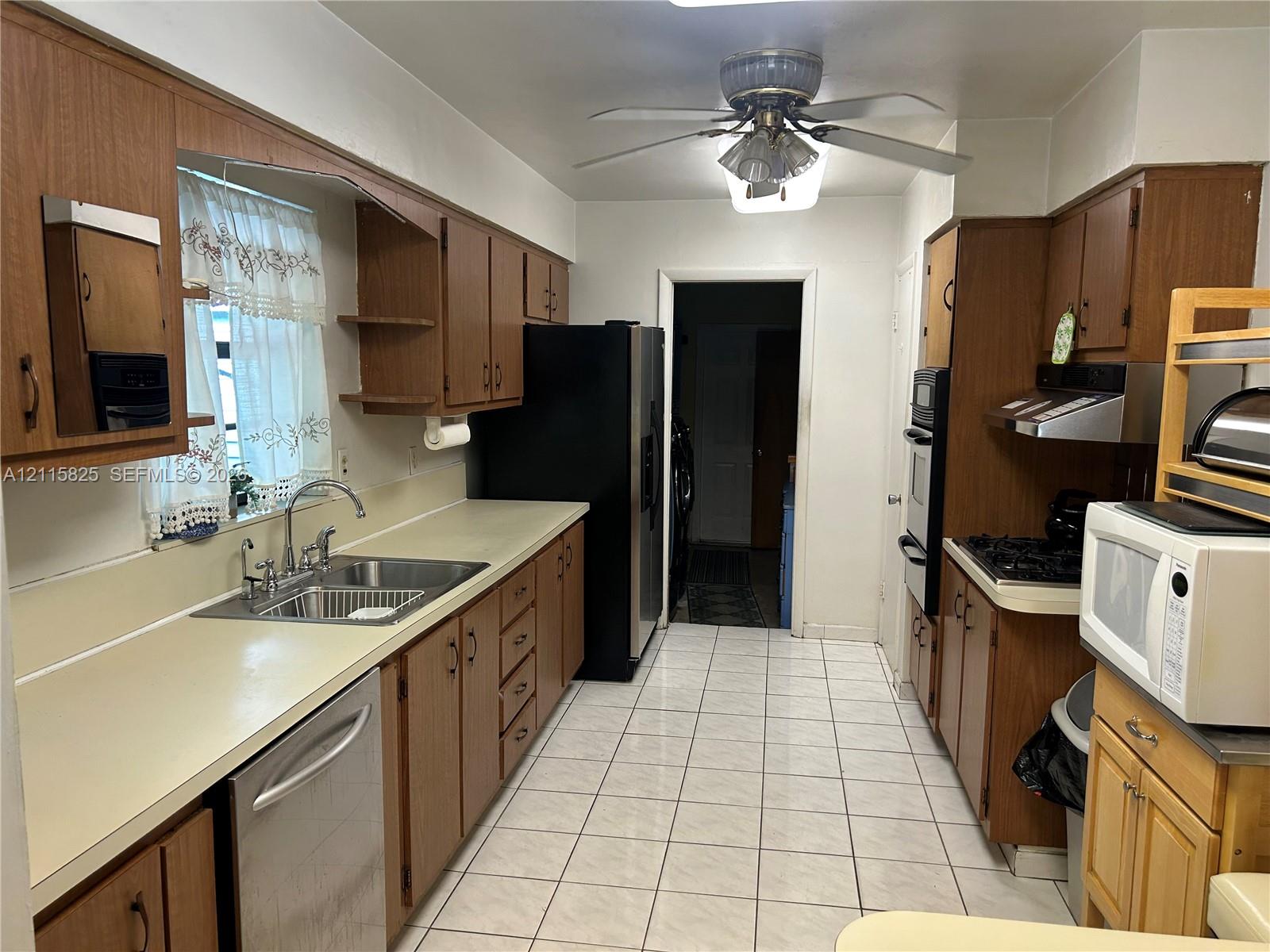 Kitchen featuring wood cabinetry, solid-surface countertops, stainless steel sink with gooseneck faucet, tile flooring, and integrated wall oven