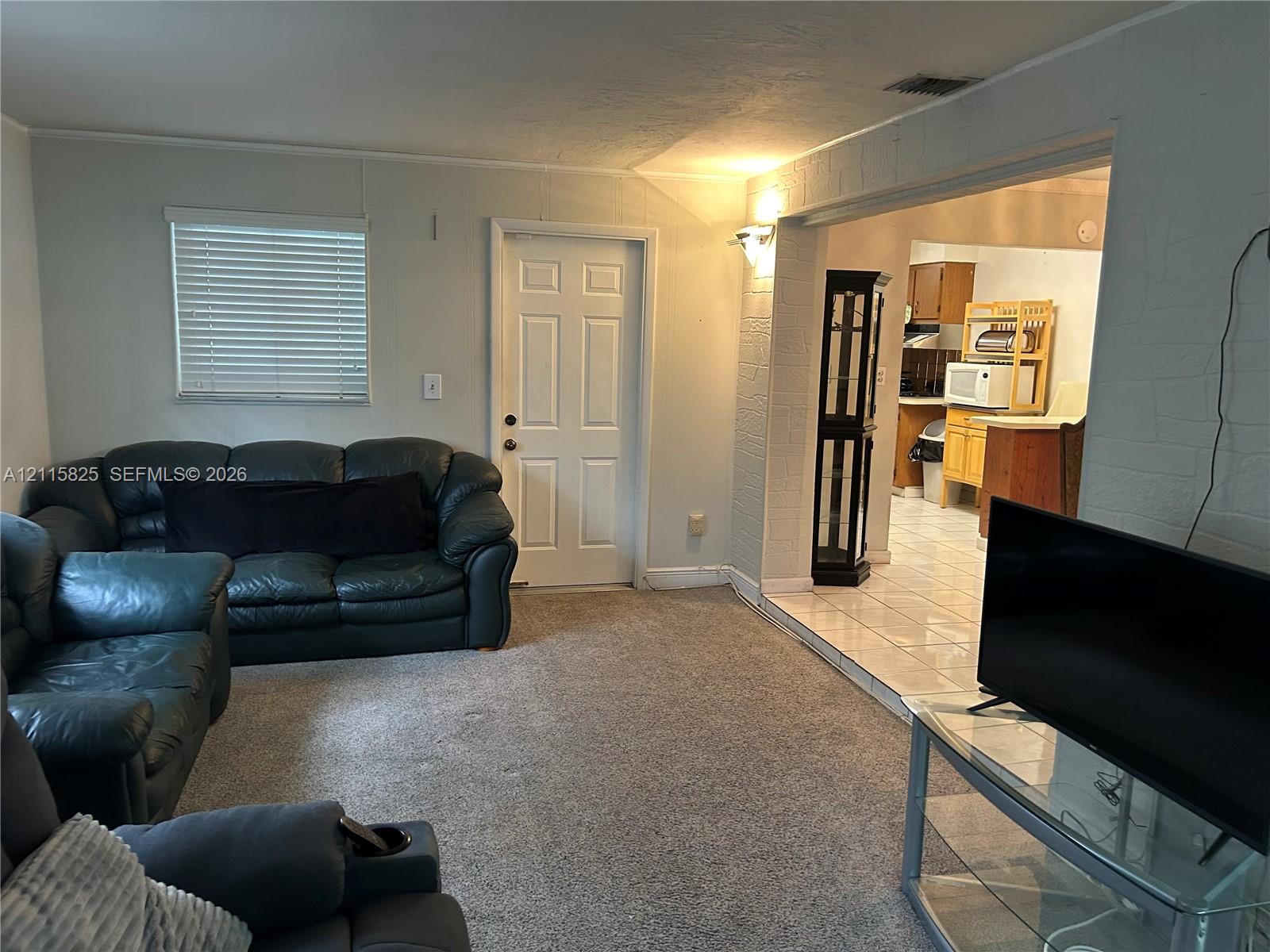 Neutral interior space featuring wall-to-wall carpeting, white textured masonry wall accents, six-panel entry door, and tiled flooring surface in the secondary area