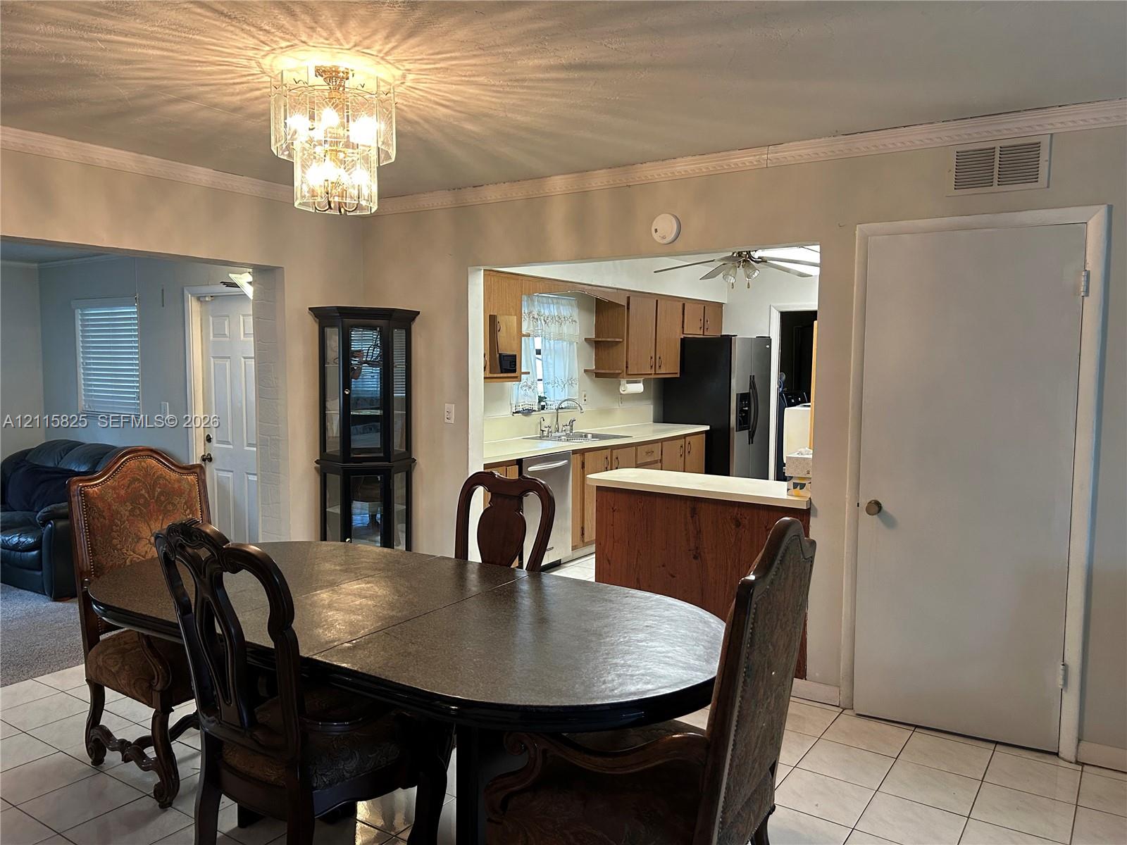 Dining area featuring a tiered crystal chandelier, tile flooring, and crown molding, with pass-through access to kitchen cabinetry and a built-in counter