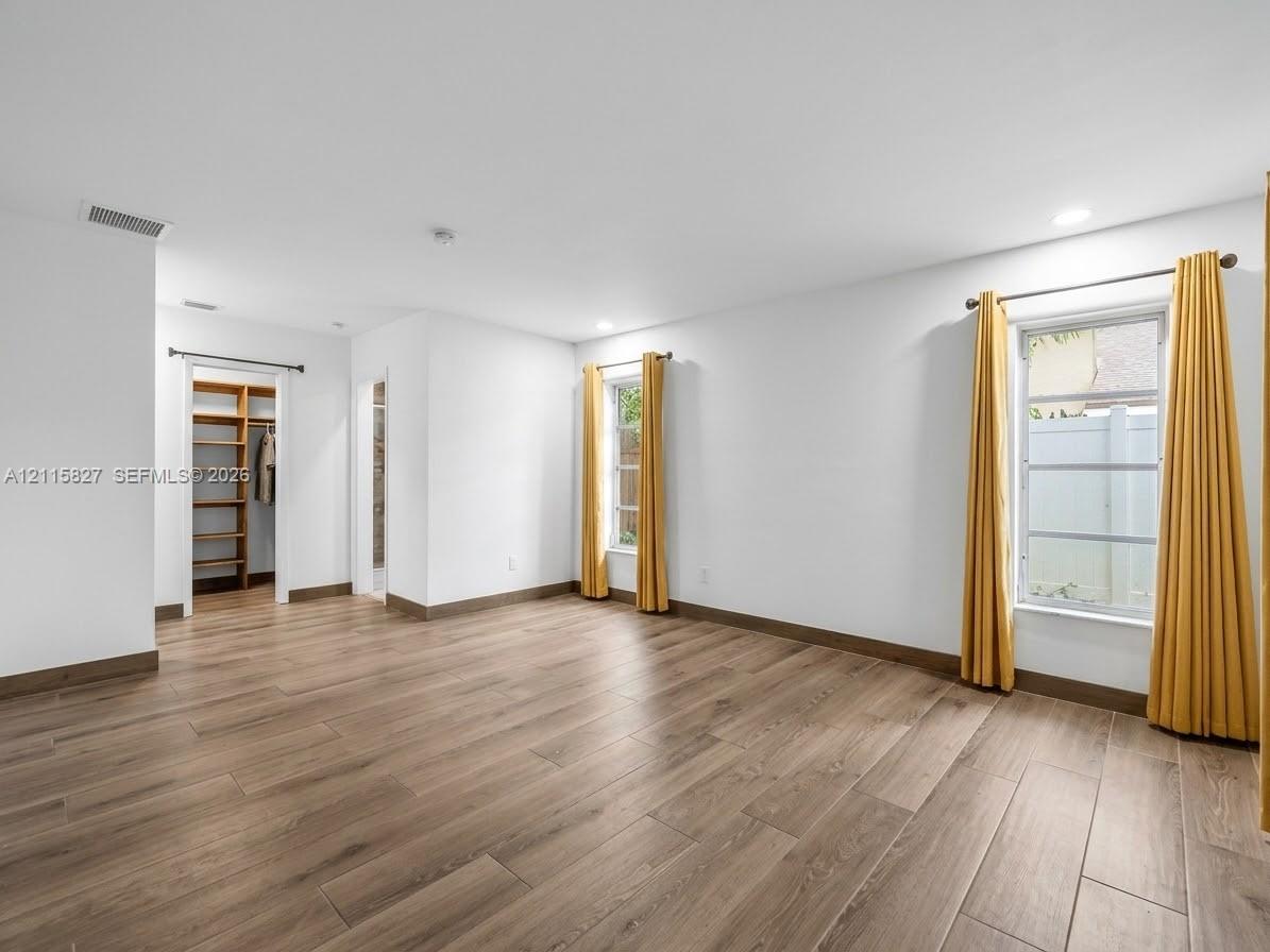 Room interior featuring wood-finish flooring, recessed lighting, and a walk-in closet with built-in wooden shelving