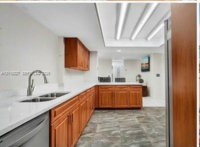 Kitchen featuring wood cabinetry, white countertops, double-basin stainless steel sink with arched faucet, recessed tray ceiling lighting, and stone-finish tile flooring