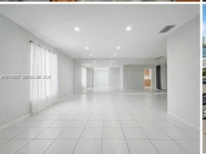 Open-concept room featuring white tile flooring, recessed ceiling lighting, and a full-length mirrored wall