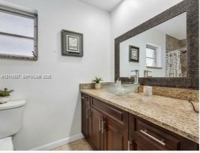 Bathroom vanity featuring a stone-finish countertop, glass vessel sink, polished chrome faucet, dark wood-finish cabinetry, and a framed mirror