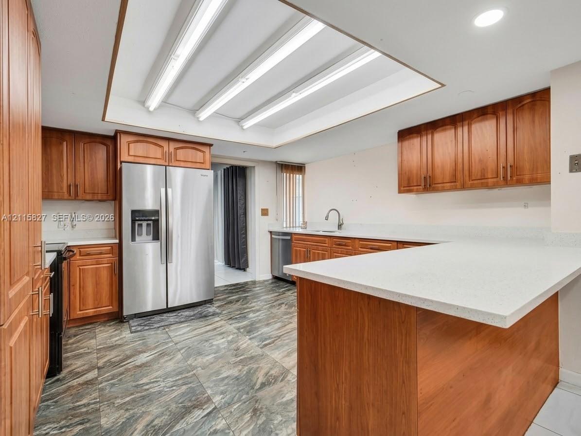 Kitchen featuring wood cabinetry, stone-finish countertops, stainless steel side-by-side refrigerator, recessed lighting, and patterned tile flooring