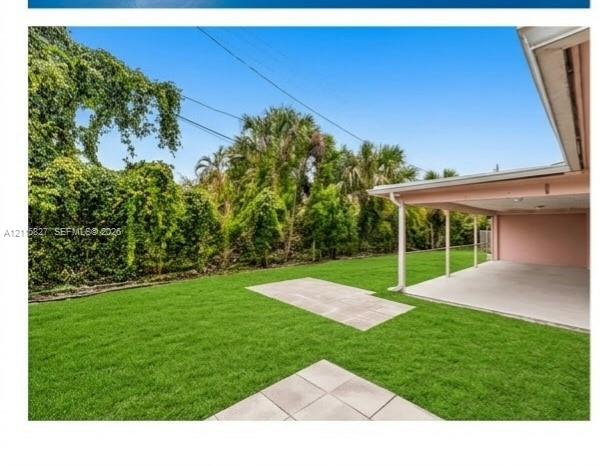 Backyard featuring a concrete patio, covered porch area, manicured lawn, and dense mature perimeter landscaping
