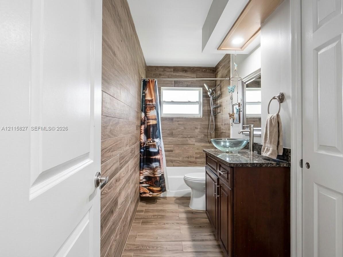 Bathroom featuring wood-finish wall and floor tile, dark wood cabinetry, a stone-surface countertop, and a glass vessel sink