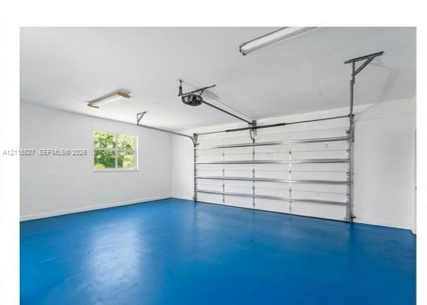 Garage interior featuring a painted concrete floor, white-finished walls, an automated sectional door, and overhead lighting