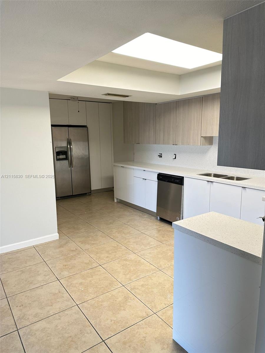 Kitchen featuring tile flooring, skylight, quartz countertops, dual-toned cabinetry, and stainless steel appliances