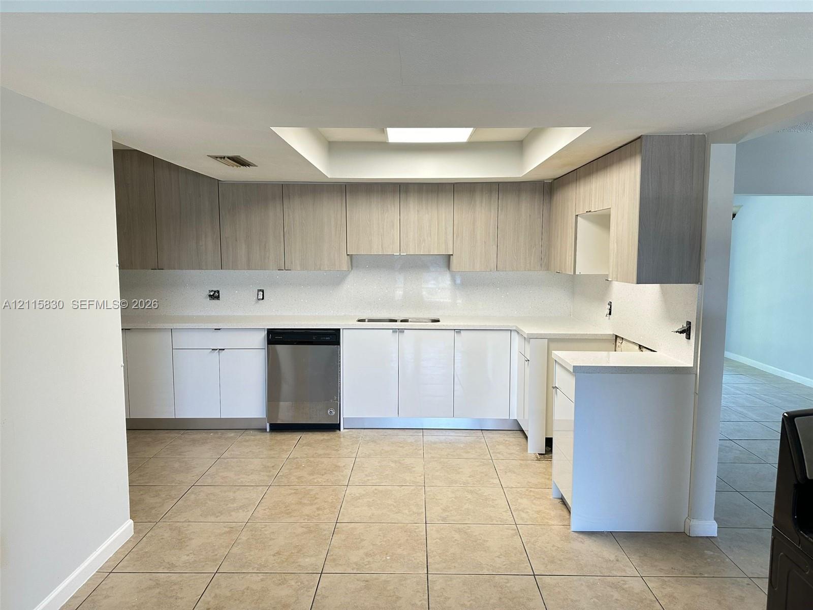 Kitchen featuring two-tone cabinetry with wood-finish uppers and white lower cabinets, solid-surface countertops, tile flooring, and built-in dishwasher