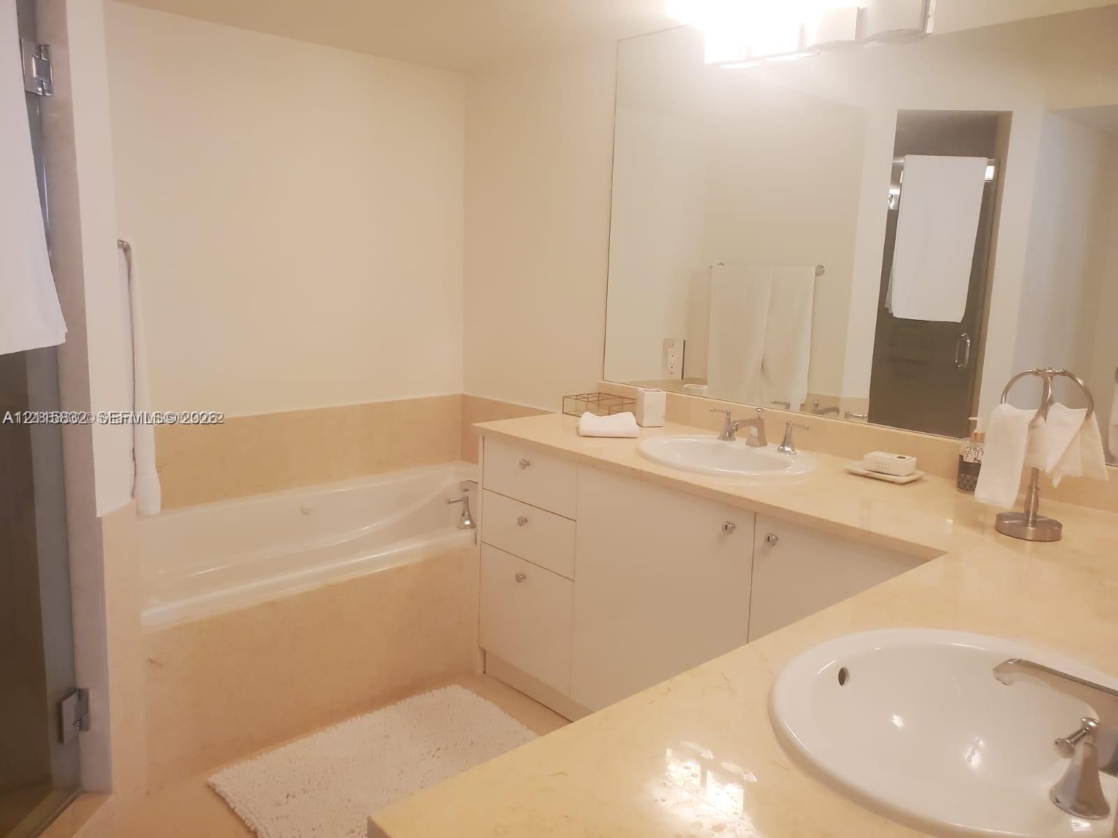 Bathroom featuring dual drop-in sinks, stone-finish countertops, built-in cabinetry, and a jetted soaking tub
