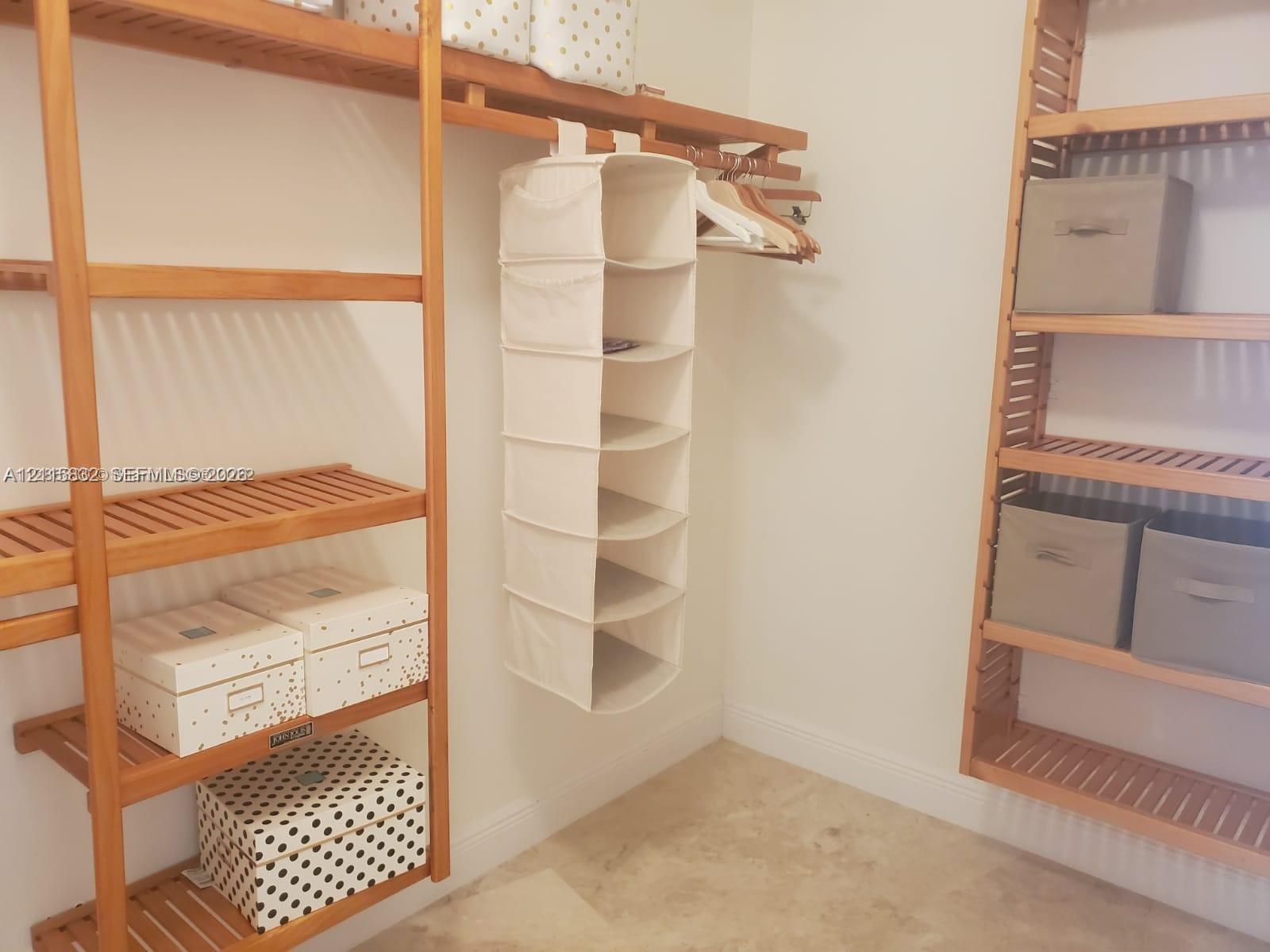 Walk-in closet featuring multi-level wooden shelving and wall-to-wall stone-finish flooring