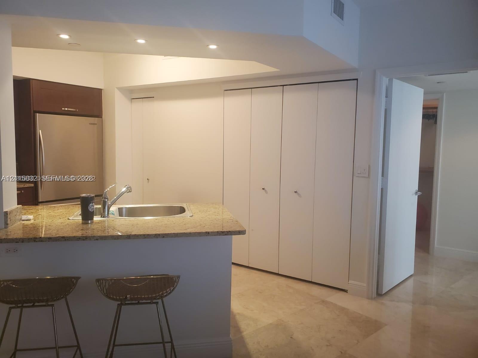 Kitchen featuring a stone-surface breakfast bar, stainless steel refrigerator, recessed lighting, and white bi-fold closet doors