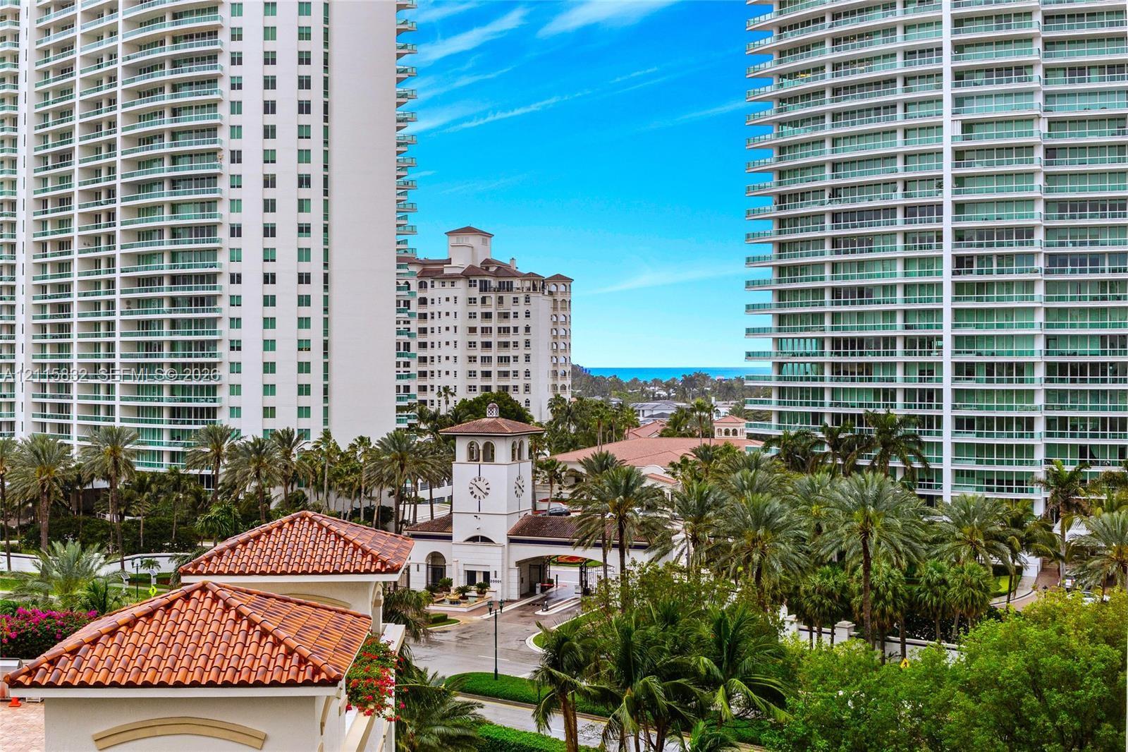High-rise towers featuring glass-paneled balconies, terracotta-tiled roof accents, clock tower architectural detail, and mature palm landscaping