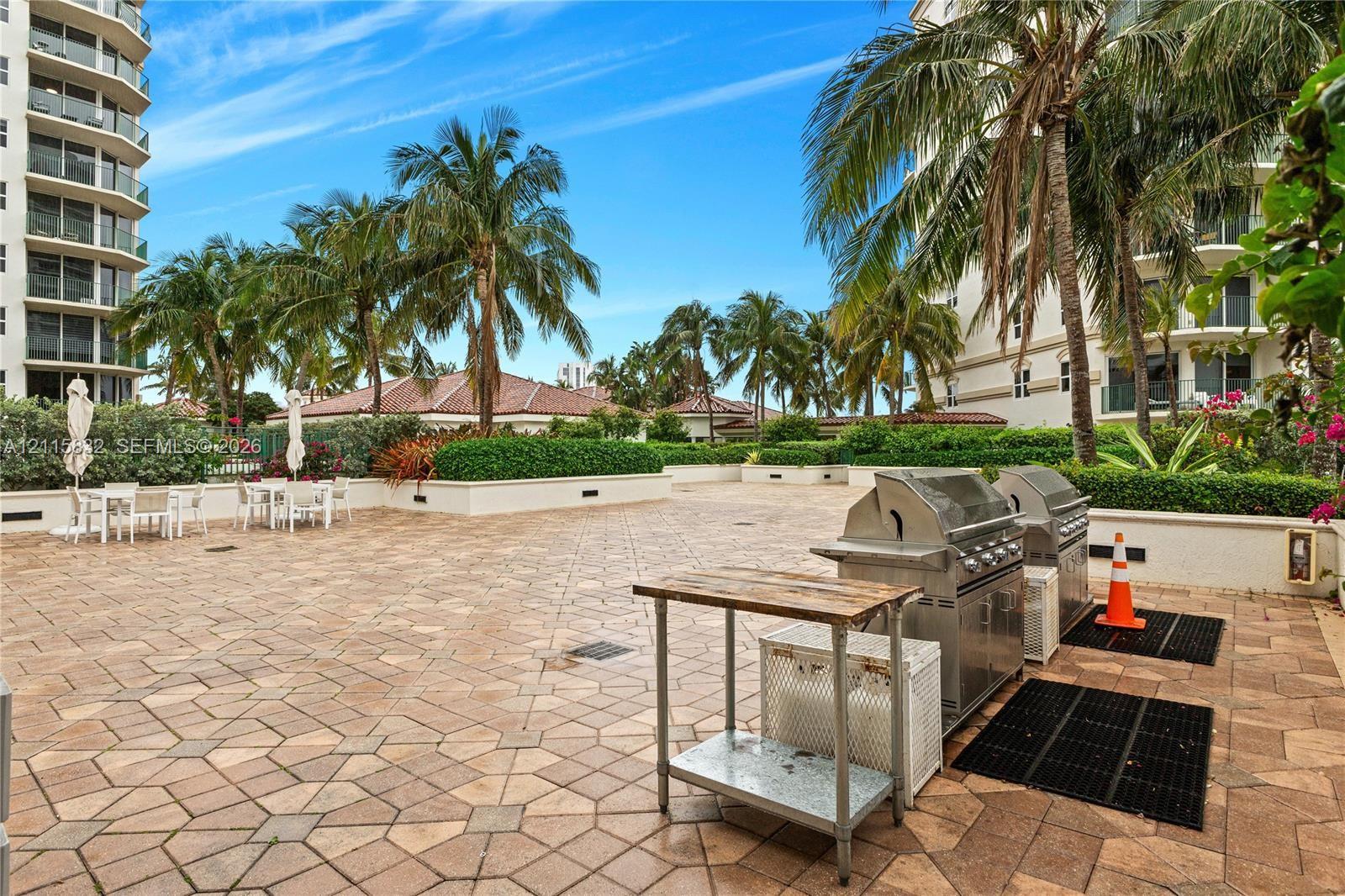Outdoor terrace featuring stone paver flooring, built-in stainless steel grilling stations, and mature palm tree landscaping