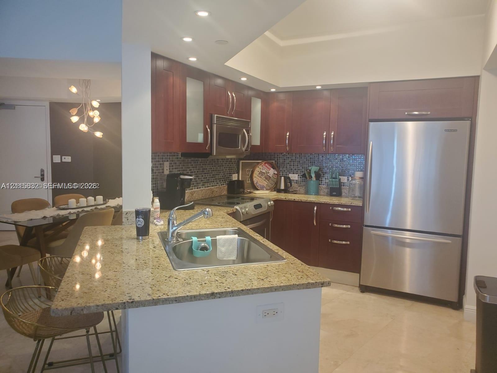 Kitchen featuring wooden cabinetry, stone-finish countertops, stainless steel appliances, recessed ceiling lighting, and a mosaic tile backsplash