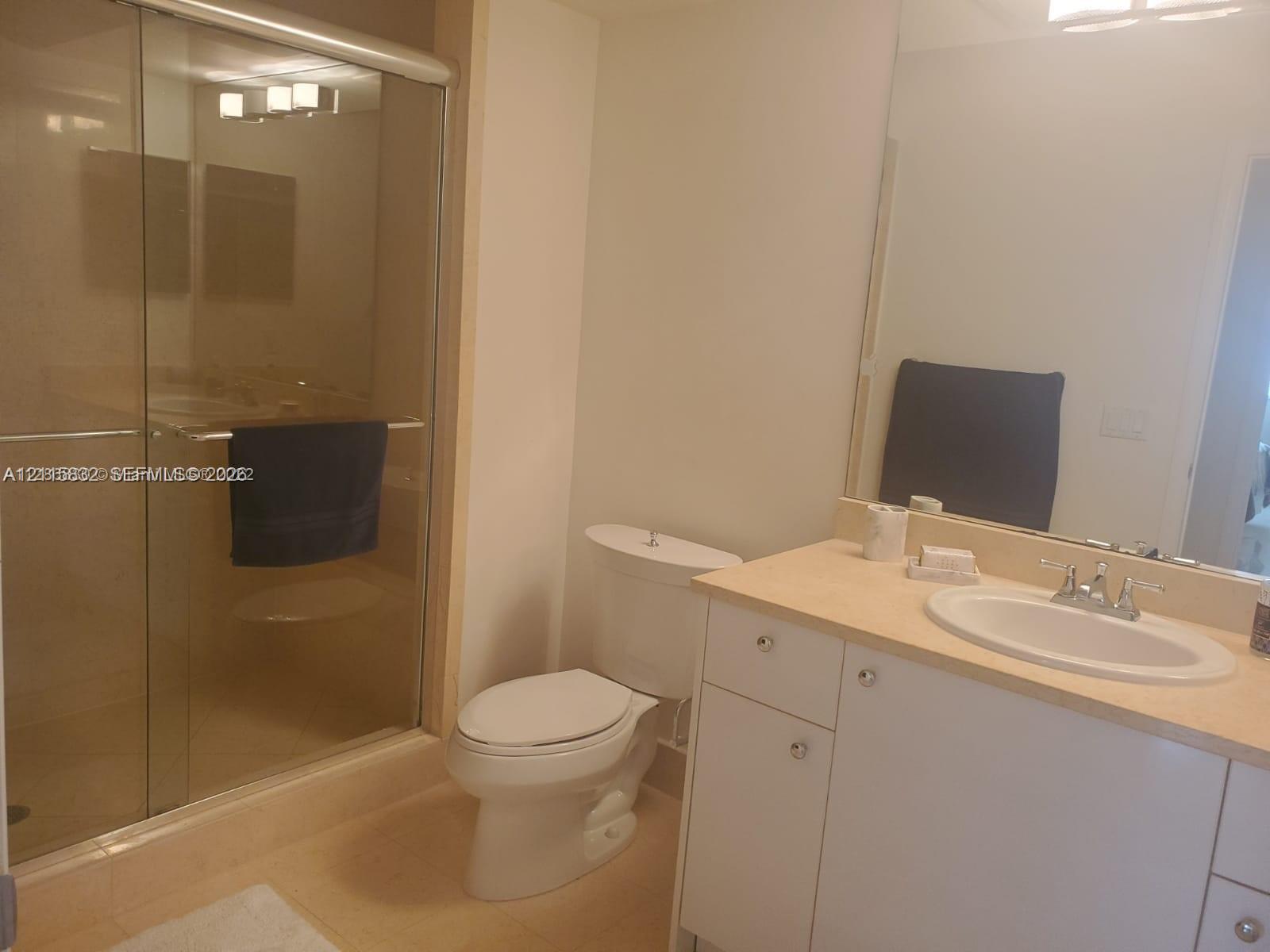 Bathroom featuring a vanity with an integrated oval sink, a large wall-mounted mirror, a two-piece commode, and a shower enclosed by sliding glass doors