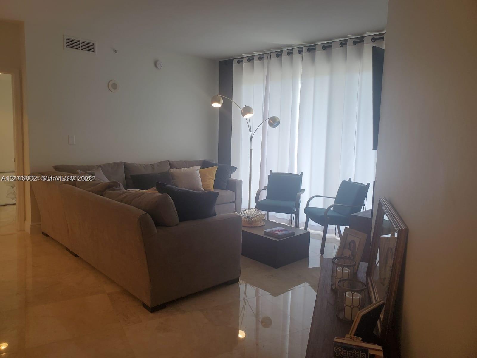 Polished stone flooring and large sliding glass doors with floor-to-ceiling curtain panels