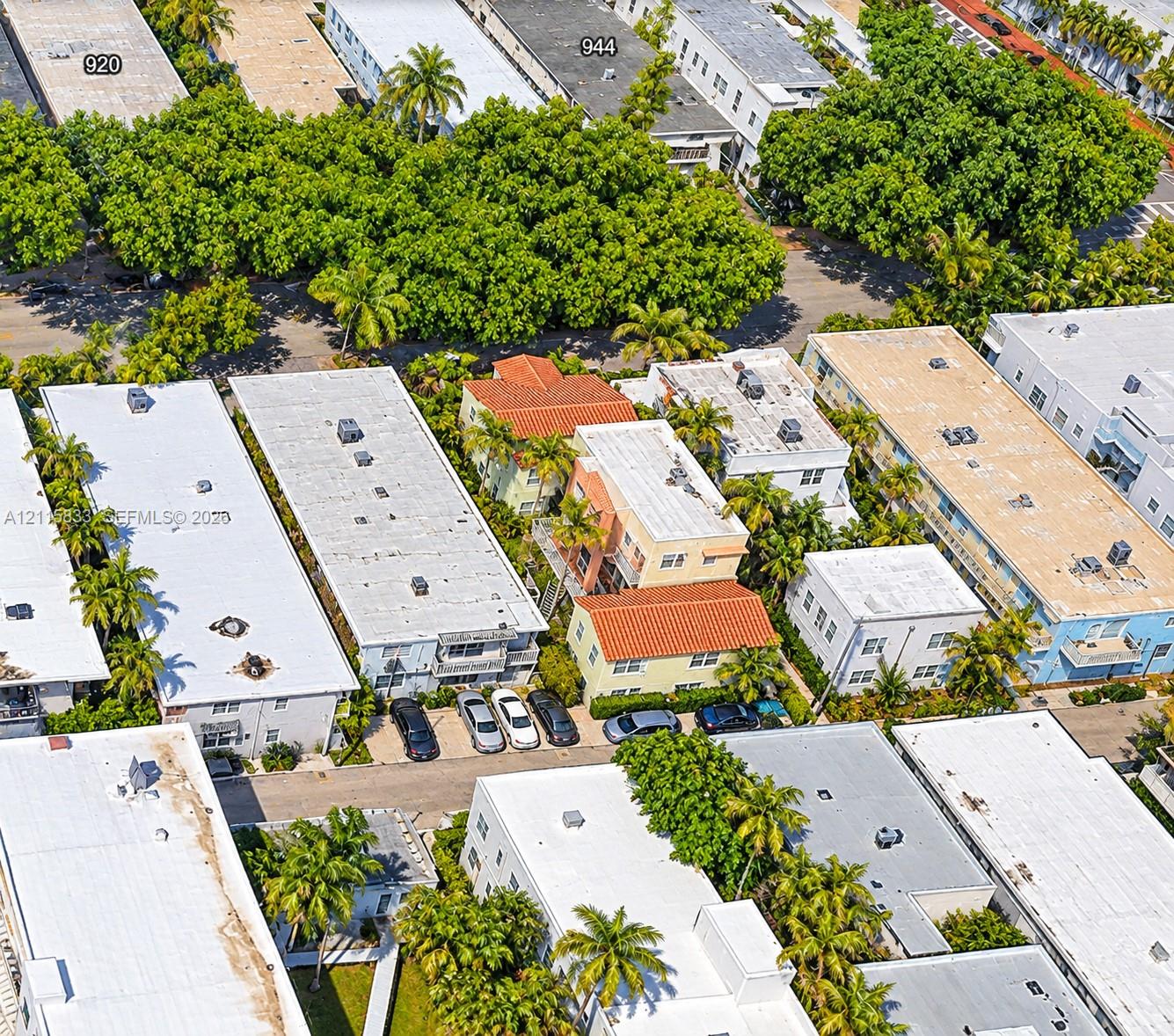Aerial perspective of a multi-unit property featuring Spanish-style architecture, terracotta roofing, mature palm trees, and designated surface parking