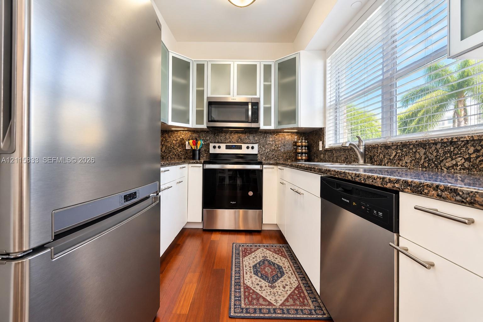 Kitchen featuring stainless steel appliances, dark stone countertops, white cabinetry with frosted glass inserts, and wood-finish flooring