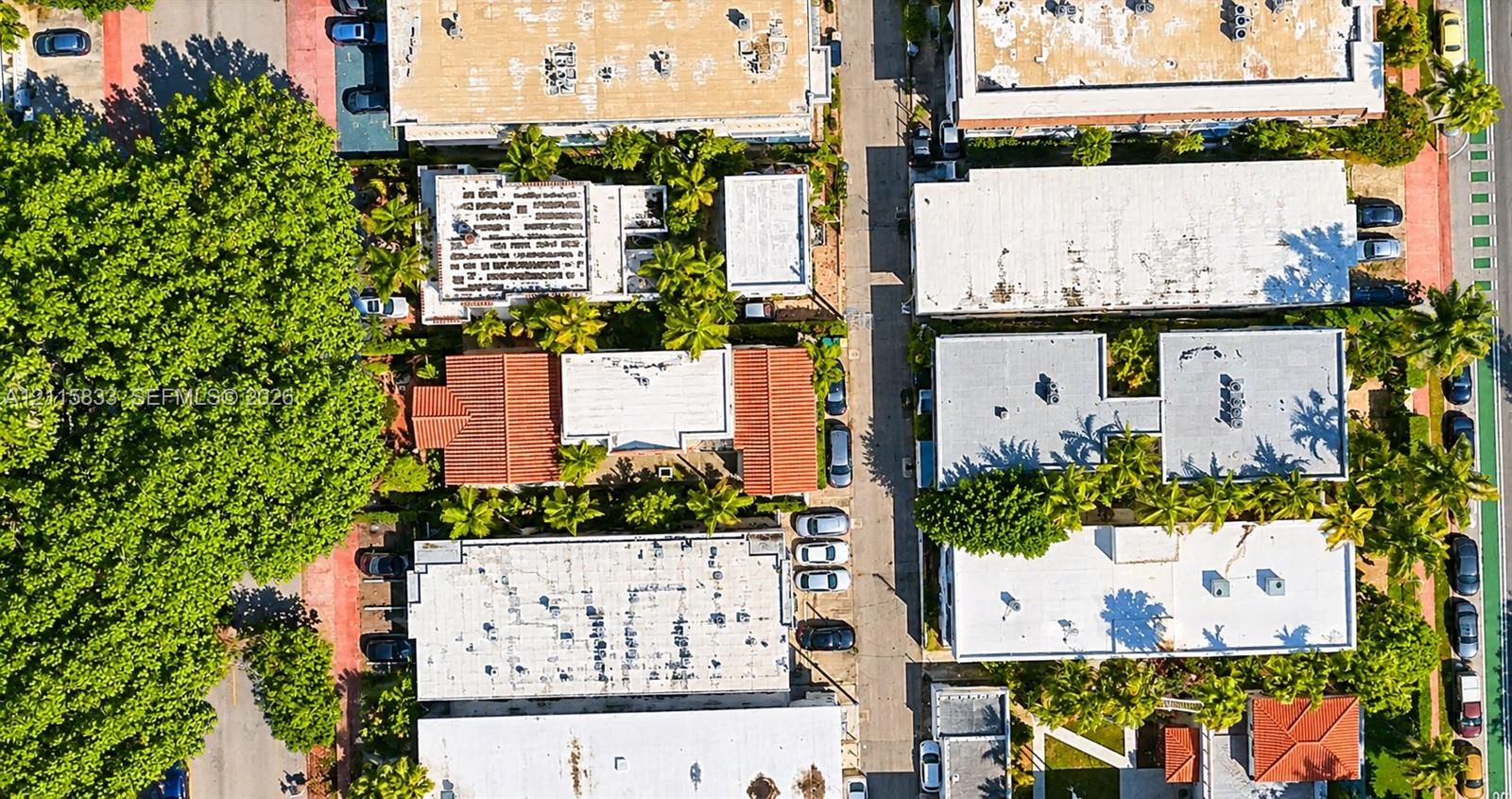 Aerial perspective of a multi-structure property featuring red clay tile roofing, onsite parking, and dense mature canopy coverage