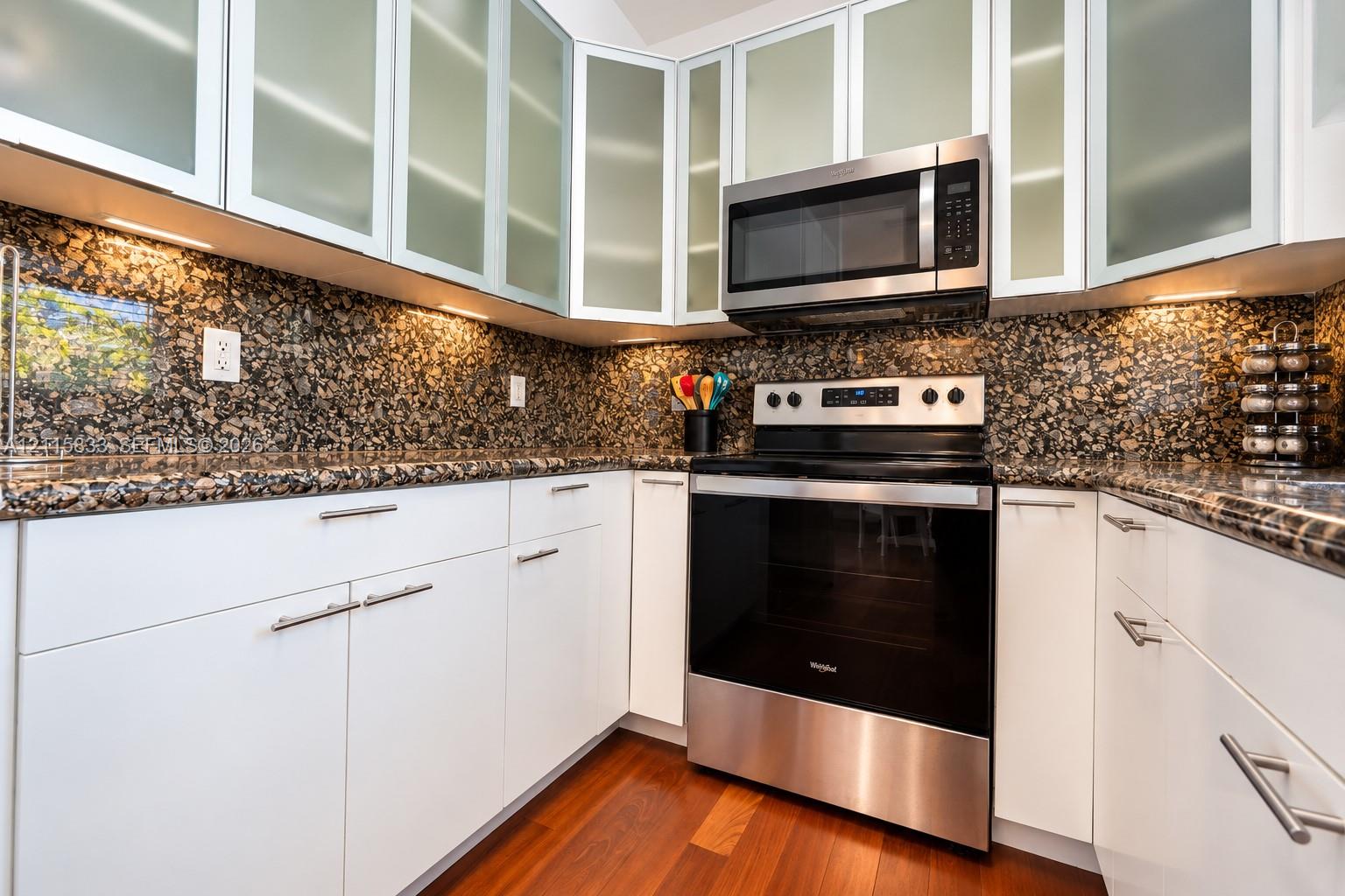 Kitchen featuring white cabinetry with frosted glass inserts, stone countertops, integrated under-cabinet lighting, stainless steel appliances, and wood-finish flooring