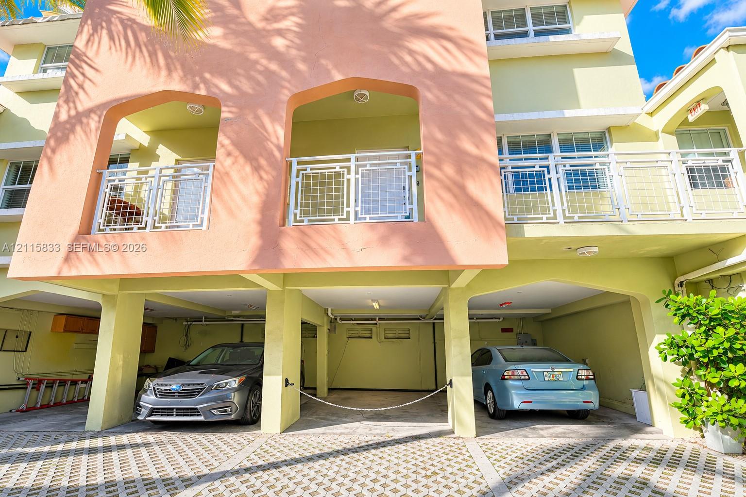 Multi-level exterior featuring stucco facade, recessed private balconies with metal railings, and covered ground-level parking with permeable paver surface