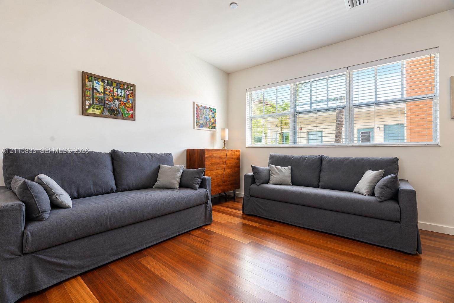 Room featuring wood-finish flooring and large windows with horizontal blinds