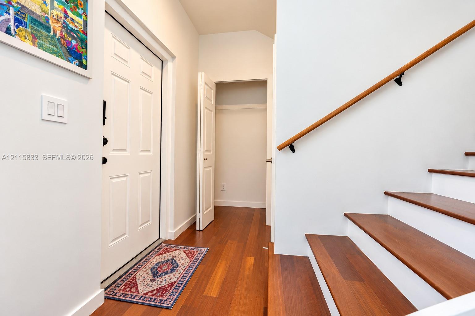 Entryway featuring wood-finish flooring, a six-panel door, built-in closet with double doors, and a staircase with wood-finish treads and a wooden handrail