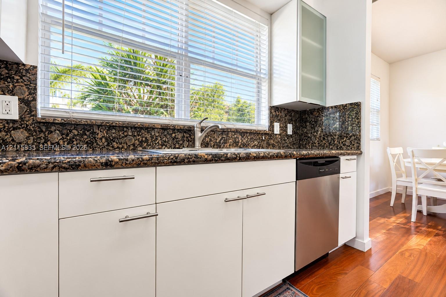 Kitchen featuring white cabinetry, stone-surface countertops with matching backsplash, stainless steel dishwasher, and wood-finish flooring