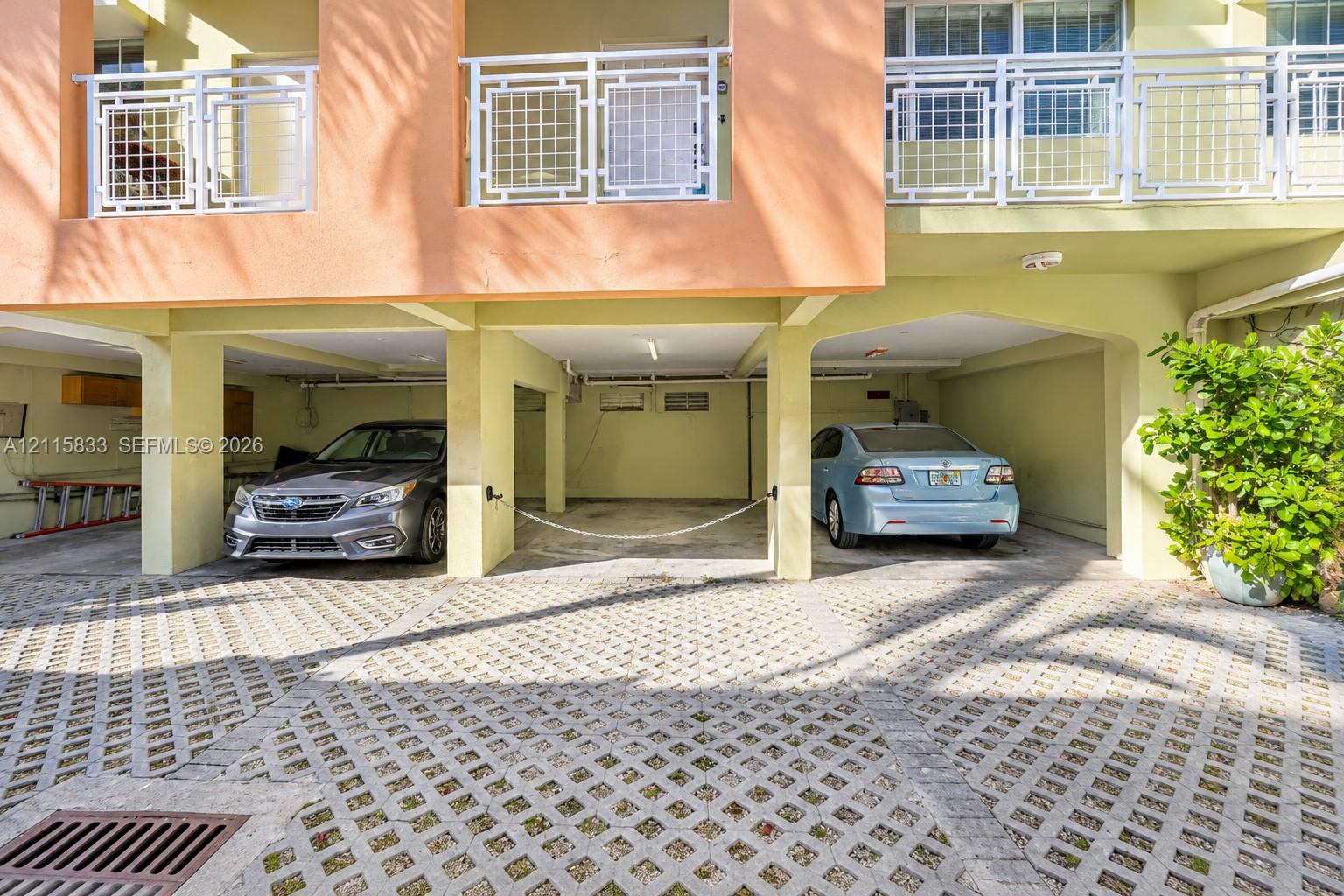 Covered parking area featuring concrete lattice pavers, structural support pillars, and upper-level balconies with white railings
