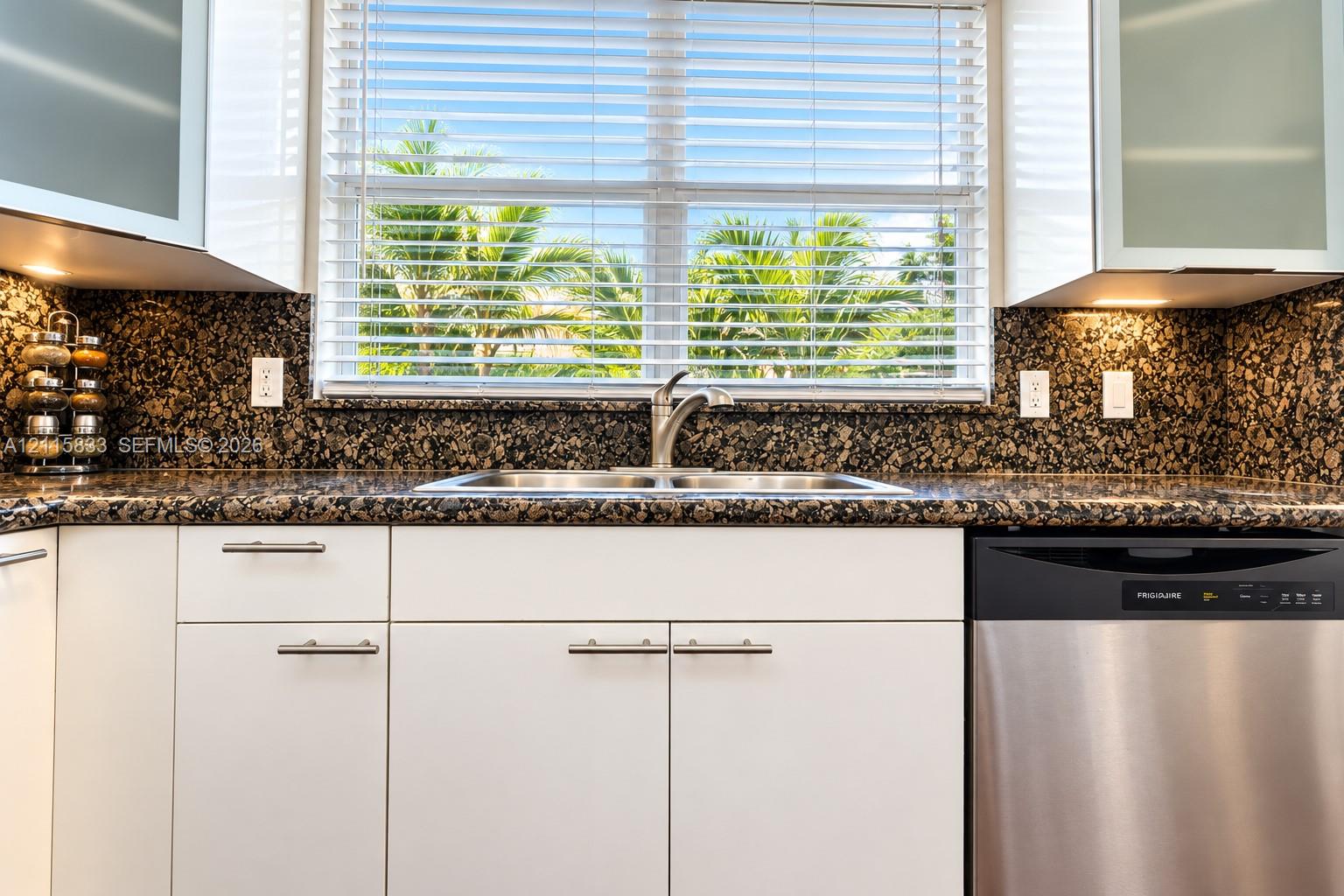 Kitchen featuring white flat-panel cabinetry, stone countertops, double-basin stainless steel sink with arched faucet, and integrated stainless steel dishwasher