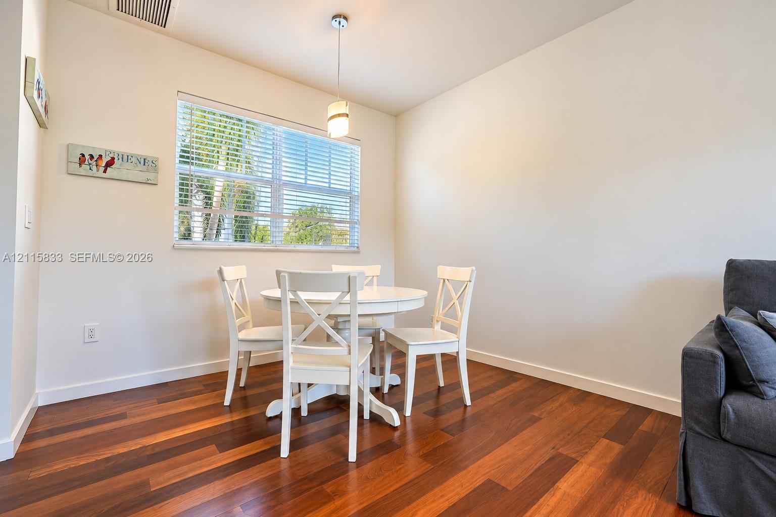 Wood-finish flooring, single-hung window with horizontal blinds, and a contemporary pendant light fixture