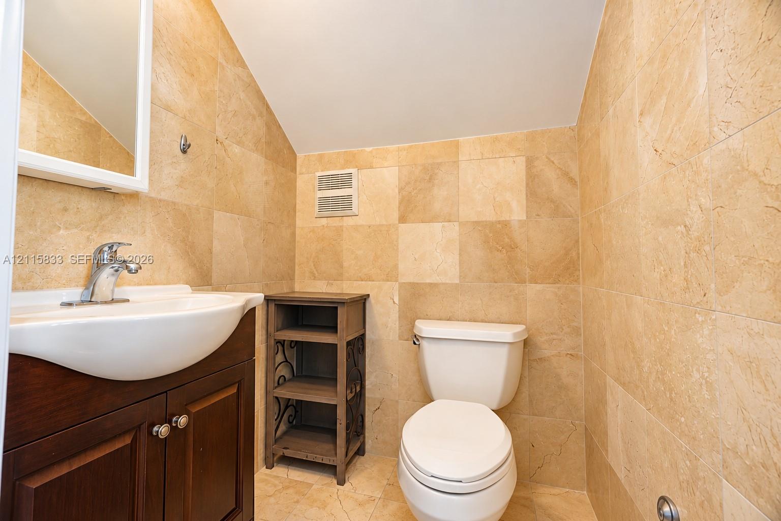 Bathroom featuring full-height stone wall tiling, wood-finish cabinetry, wall-mounted mirror, and a ceramic pedestal sink