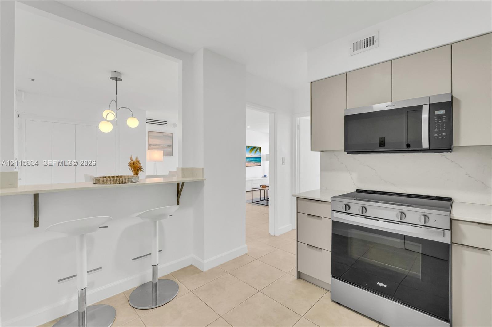 Kitchen featuring flat-panel cabinetry, a quartz countertop with a matching backsplash, stainless steel appliances, and a breakfast bar