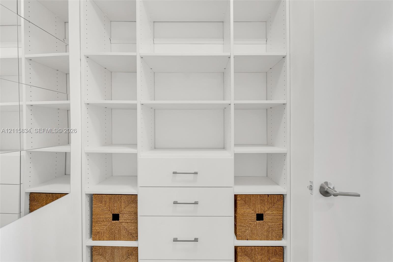 Custom white built-in shelving featuring adjustable dividers, integrated drawers with metallic hardware, and a mirrored side panel