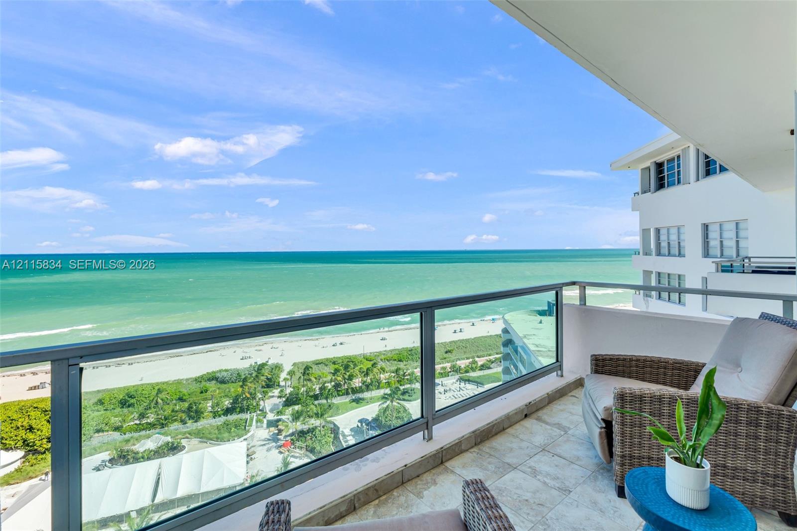 Covered balcony featuring stone tile flooring and a glass panel railing with a direct ocean and beach vista
