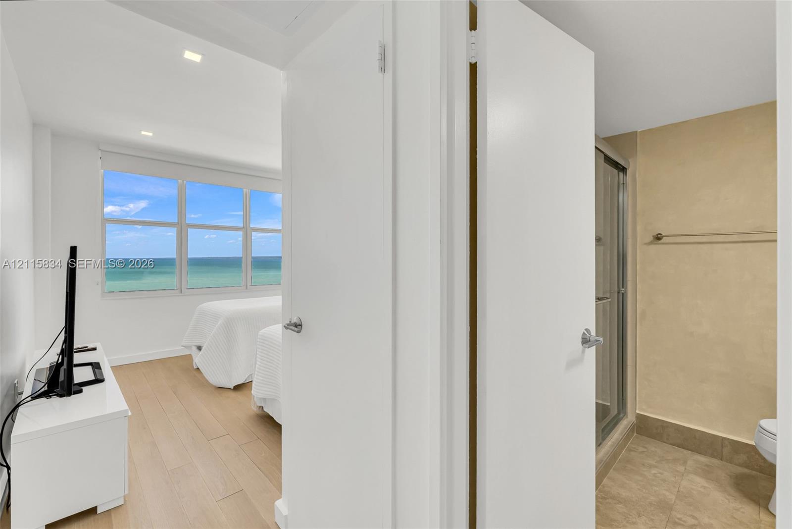 Expansive window with ocean scenery, wood-finish flooring, recessed lighting, and a walk-in shower with tile surround