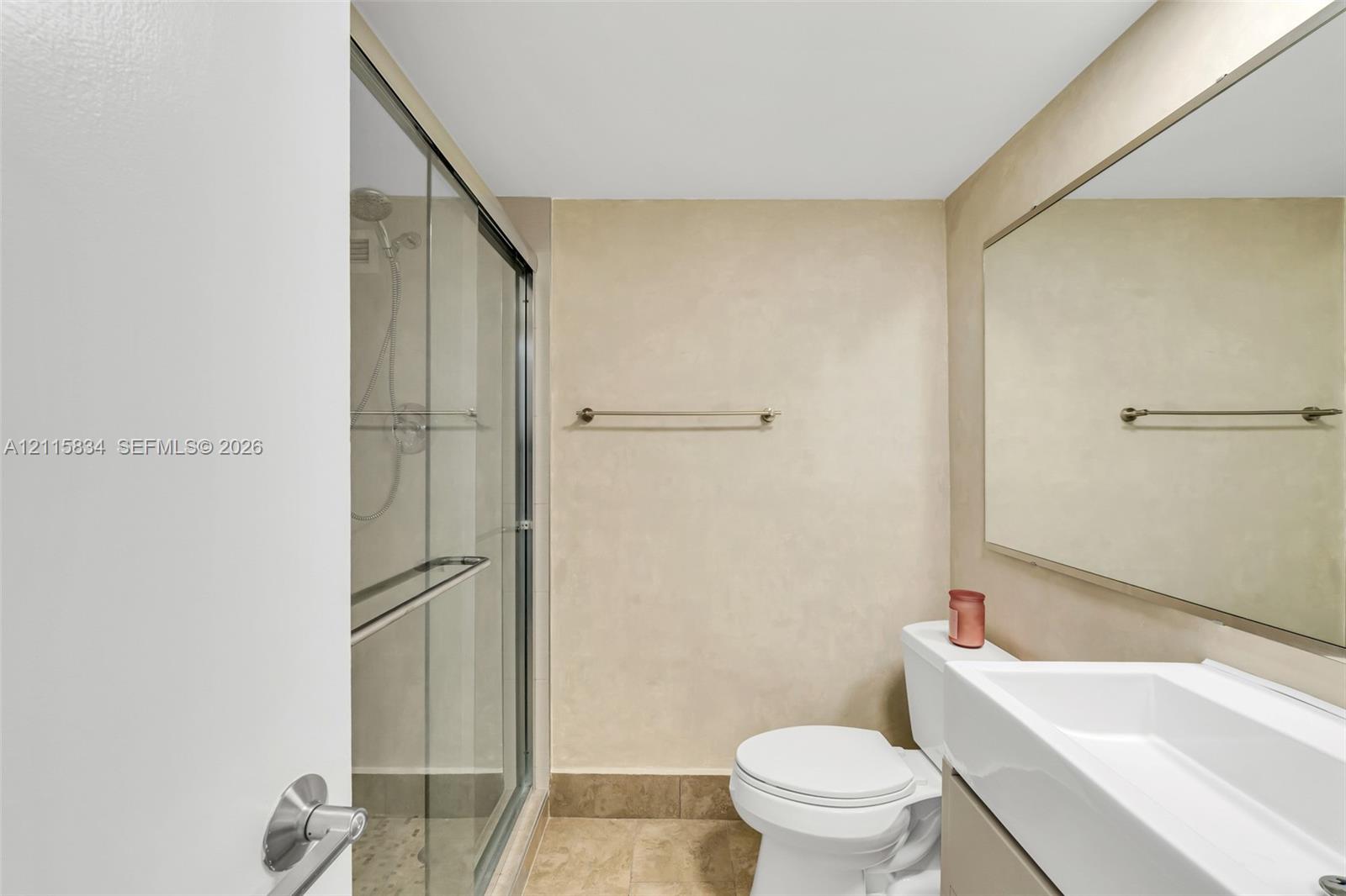 Bathroom featuring a walk-in shower with a glass enclosure, a wall-mounted mirror, a rectangular vessel sink with a vanity, and a neutral-toned tile floor