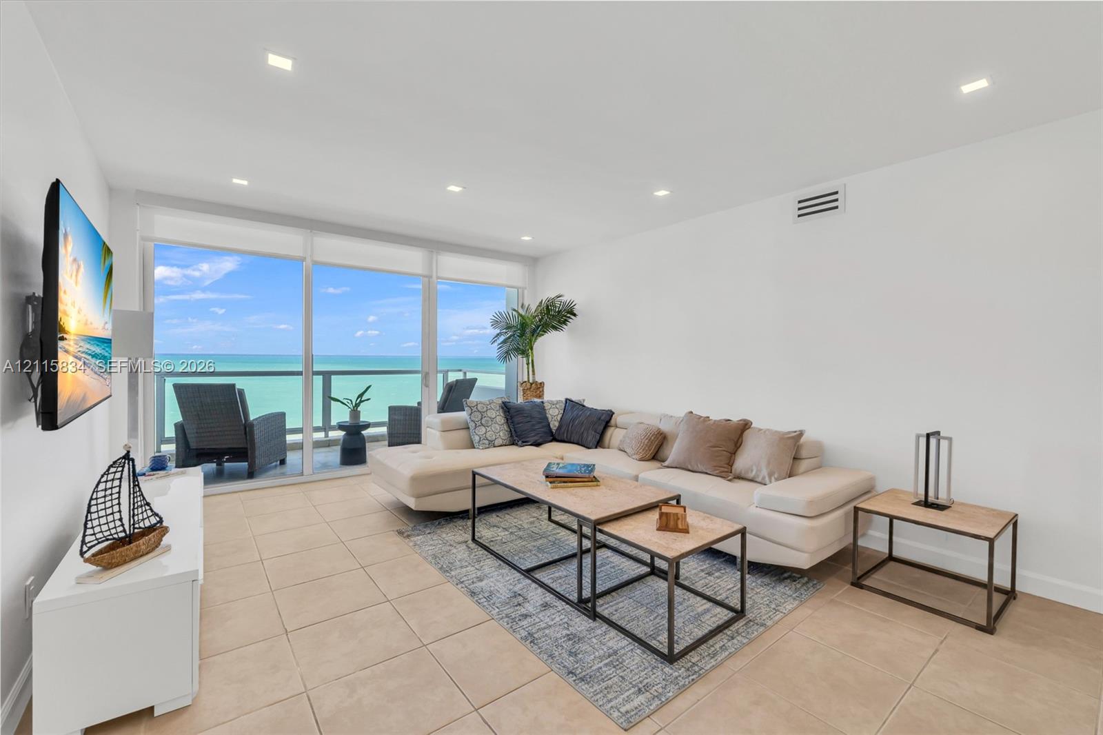 Living area featuring ceramic tile flooring, recessed lighting, and floor-to-ceiling glass sliding doors opening to a private balcony with ocean frontage