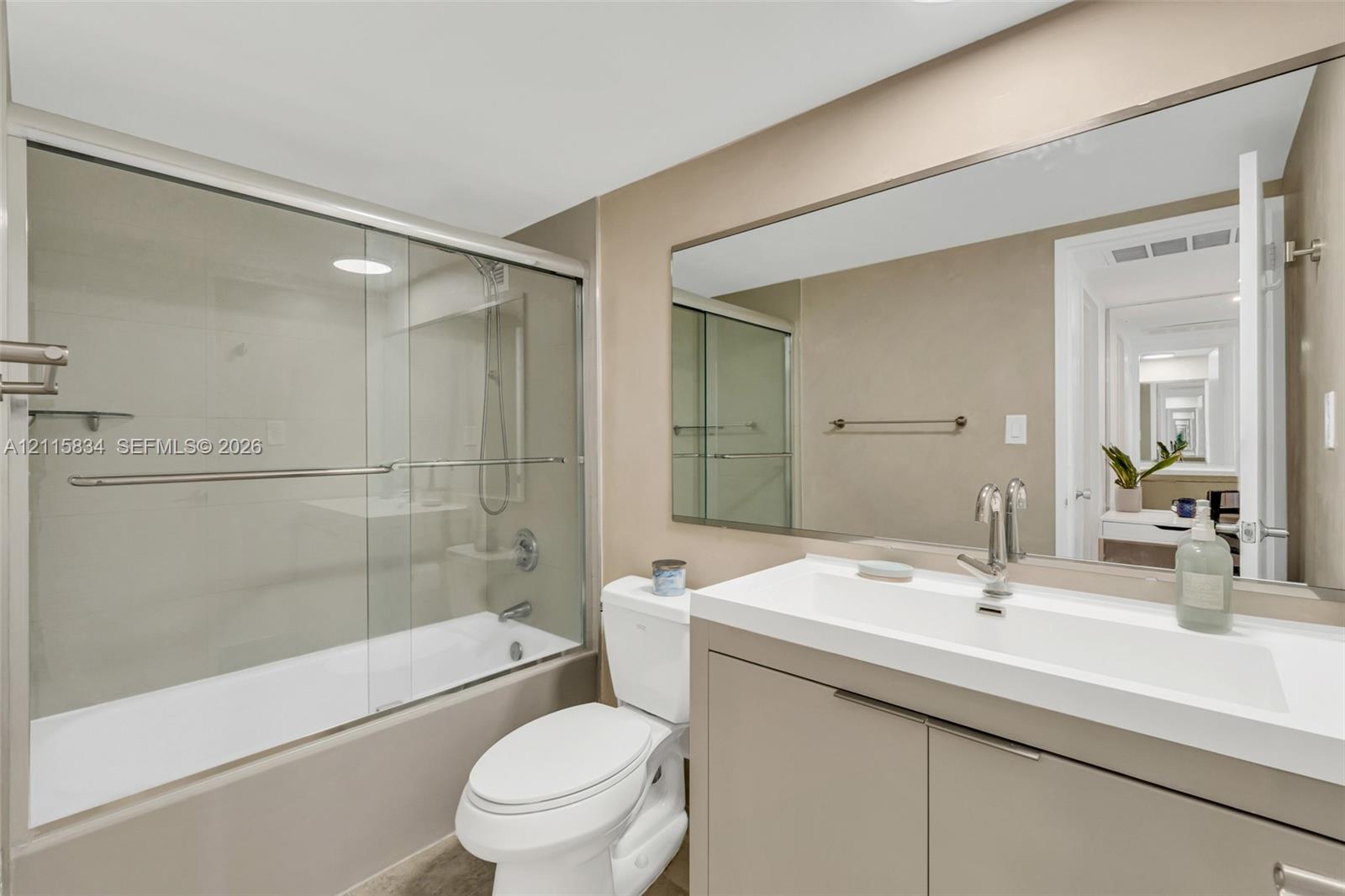 Bathroom featuring a floating vanity with an integrated sink, large wall-mounted mirror, glass-enclosed shower and tub combination, and chrome fixtures