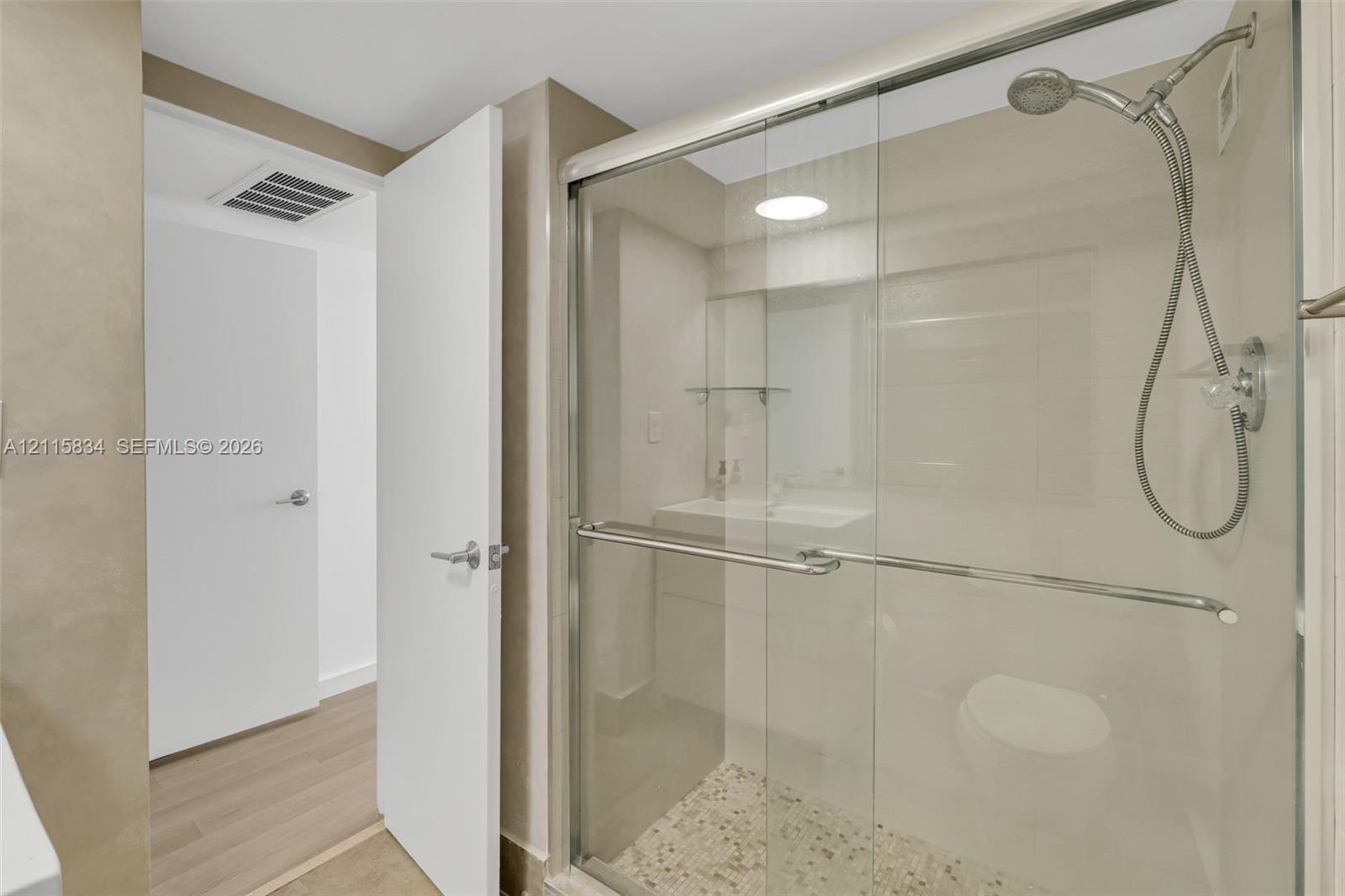 Walk-in shower with a glass enclosure, polished metal hardware, handheld showerhead, and pebble-style floor tiling
