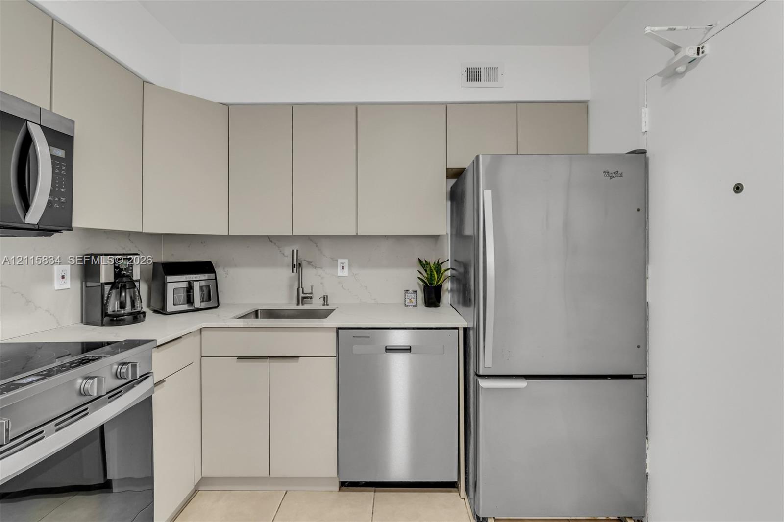 Kitchen featuring flat-panel cabinetry, stainless steel appliances, light-toned countertops with a matching backsplash, and tile flooring