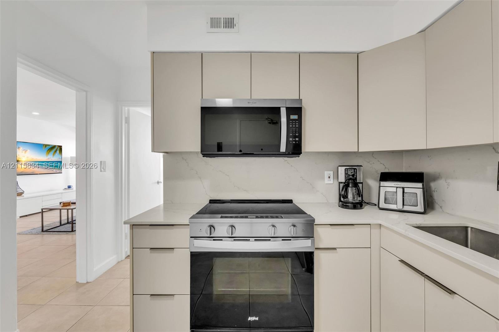 Kitchen featuring flat-panel cabinetry, light-toned stone-finish countertops, full-height stone-finish backsplash, and stainless steel appliances